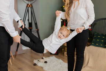 Happy dad and mom swing their daughter in their arms.