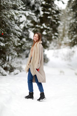 happy young woman in winter day outdoors in forest. background of tree branches in the snow and decorated with Christmas decorations.