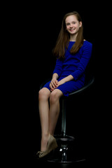 Fototapeta na wymiar Charming girl teenager sitting on a chair in the studio on a bla