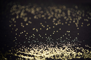 Beautiful Christmas light background. Abstract glitter bokeh and scattered sparkles in gold, on black