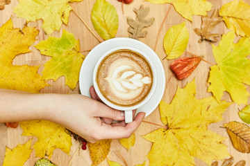 Autumn flat lay composition with dry leaves wreath frame and coffee latte cup in woman hand on wood background. 