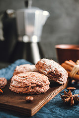Chocolate cookies, cup with coffee, moka pot, cinnamon sticks, star anise on blue napkin, dark background with copy space