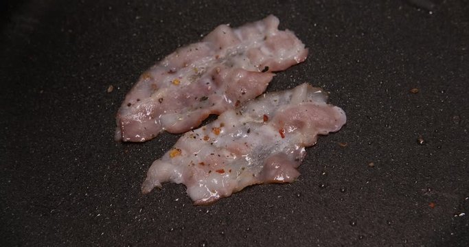 Two thin slices of meat lie in frying pan, butter squid, high temperature, frying bacon for breakfast, spices sprinkled on bacon, unprofitable breakfast, all the most delicious is very unhealthy, fat