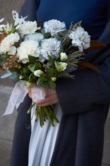 Close-up female hands holds white toned bouquet in vintage style outdoors on a gray wall background, selective focus