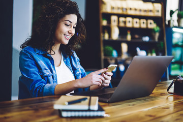 Cheerful hipster girl dressed in casual wear reading received email from friend in social networks...
