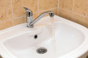 Sink with a chrome tap from which a stream of water flows, white washbasin.