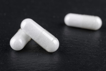 white capsules of nutritional supplement msm, sulfur on black background