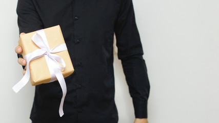 Man offering or showing a gift for someone. Happy young hipster with a gift in hands. Celebration background with a guy holding a box with a ribbon. Surprise concept..