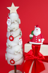 Gypsum colorful santa claus on the gift box and christmas tree with decorations over red background.