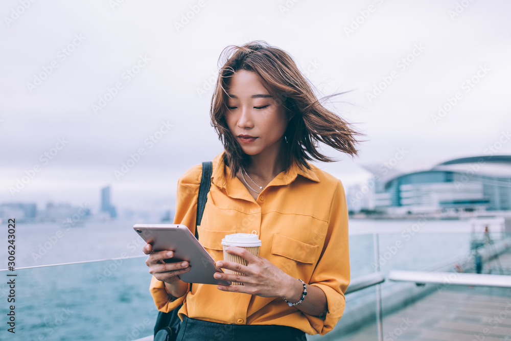 Poster beautiful japanese hipster student checking received notification on modern touch pad standing at ur