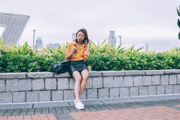 Obraz premium Trendy Asian woman sitting texting at street