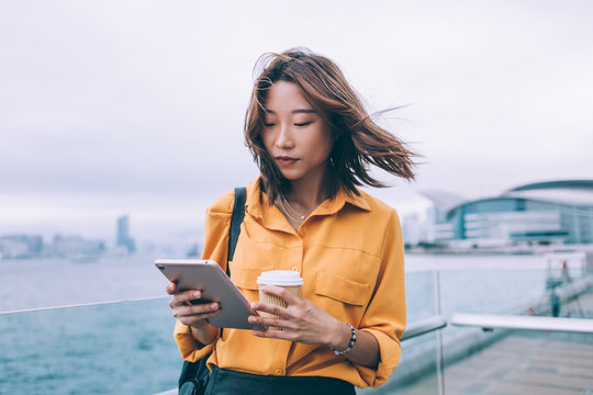 Beautiful Japanese hipster student checking received notification on modern touch pad standing at urban setting and using public internet connection for installation, millennial woman testing app