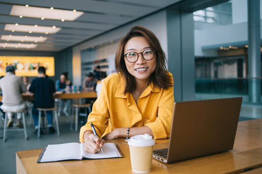 Cheerful female working on laptop and taking notes