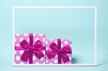 Two present boxes with dots  wrapped with bright ribbon on colorful background with white frame. Festive and holiday theme.