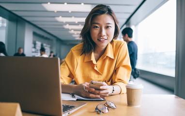 Female student using smartphone at desk at coffee break