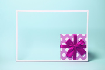 Present boxe with dots  wrapped with bright ribbon on colorful background with white frame. Festive and holiday theme