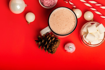 Cup of hot cocoa and marshmallows with christmas candy canes on a red background. White christmas tree decorations and candies.