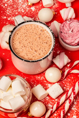 Cup of hot cocoa and marshmallows with christmas candy canes on a red background. White christmas tree decorations and candies.