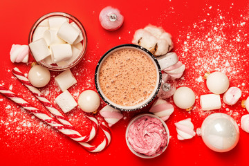Obraz na płótnie Canvas Cup of hot cocoa and marshmallows with christmas candy canes on a red background. White christmas tree decorations and candies.
