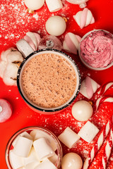 Cup of hot cocoa and marshmallows with christmas candy canes on a red background. White christmas tree decorations and candies.