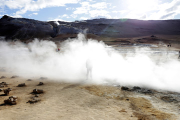 Tourist in volcanic area, Iceland.  Boiling mudpots in the geothermal area Hverir and cracked ground around. Location: geothermal area Hverir, Myvatn region, North part of Iceland, Europe 