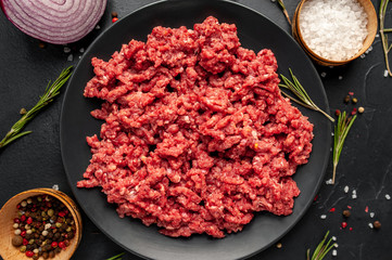 Fresh raw minced beef with herbs and spices on a black plate on a stone background