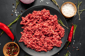 Fresh raw minced beef with herbs and spices on a black plate on a stone background