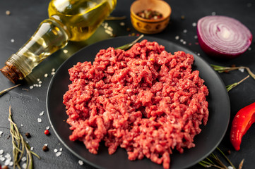 Fresh raw minced beef with herbs and spices on a black plate on a stone background