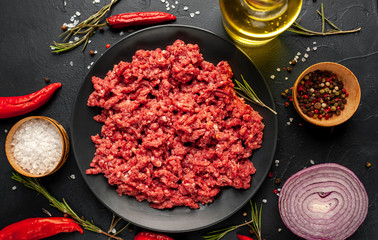Fresh raw minced beef with herbs and spices on a black plate on a stone background