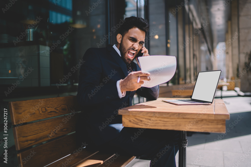 Poster angry turkish man in formal wear feeling rage while checking data from accounting report calling to 
