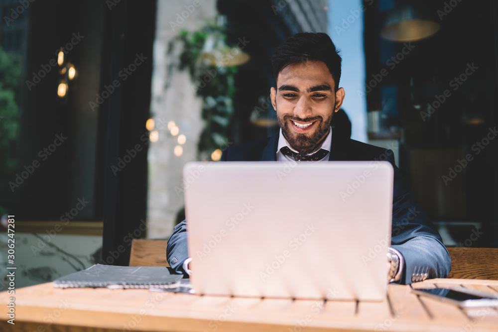 Poster positive turkish male trader working with calculations via laptop application while sitting in stree