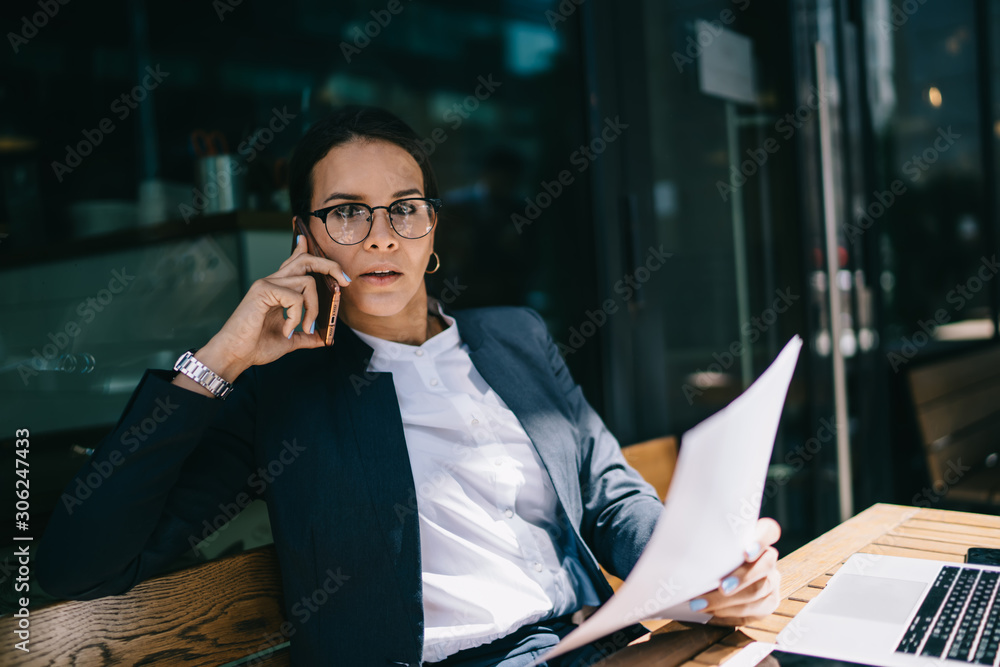 Poster portrait of financial expert in optical eyeglasses looking at camera while discussing details of bus