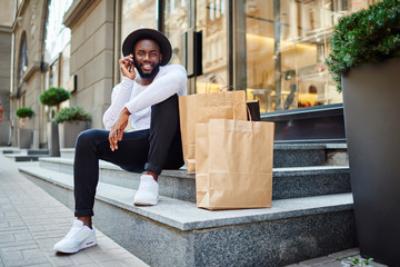 Happy afro american male buyer in trendy wear calling to friend for communicate about successful...