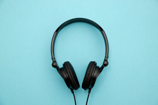 A pair of black stylish headphones with wires lie on a blue background in the middle.