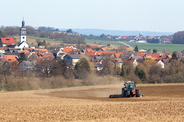 tractor plowing field and landscape with houses © Anselm