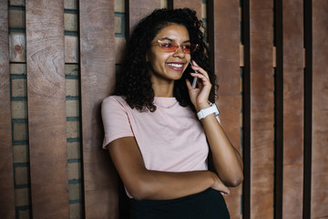 Positive female teenager in pink sunglasses with cool chanterelles design smiling while phoning to best friend using roaming internet connection on cell smartphone, stylish woman calling via app