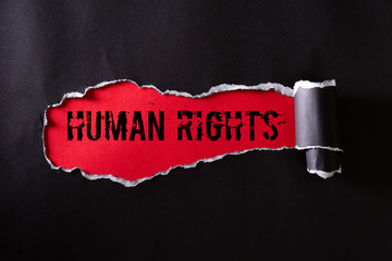 Top view of Black torn paper and the text HUMAN RIGHTS on a red background. Human rights concept.