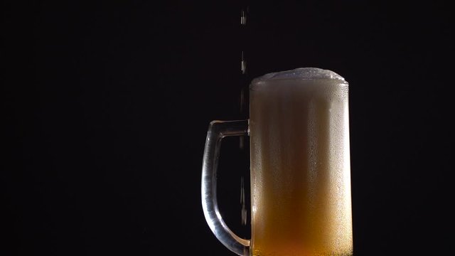 Beer is pouring into glass. Cold Light Beer in a glass with water drops. Craft Beer forming waves close up. Freshness and froth. Slow motion. Black background. Microbrewery craft beer.