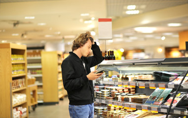 Young man shopping in supermarket, reading product information	