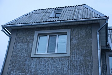 a large window on a gray attic wall under a slate roof against a gray evening sky