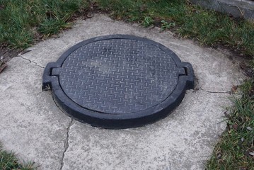 black iron hatch on the sewer in gray concrete on the street