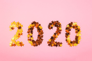 2020 new year lined with numbers from golden glowing stars on a bright pink background. Winter holidays and christmas concept. Top view, flat lay.