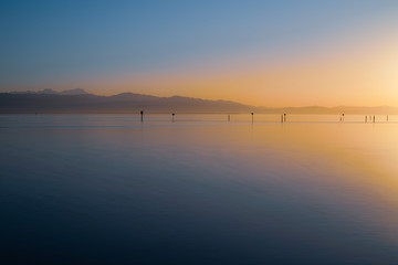 magical, atmospheric and colorful sunset on the lake with view of the mountains and lsmooth surface of water (switzerland, germany, lake of constance)