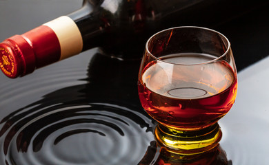 Bottle of red wine with wineglass. Water splash and droplet on the black reflection.