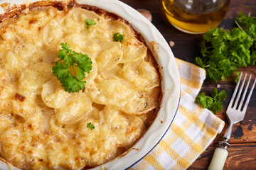 Potato gratin. Slices of potato backed with cream sauce, garlic and cheese, decorated with parsley leafs. Rustic style. Vegetarian dish.