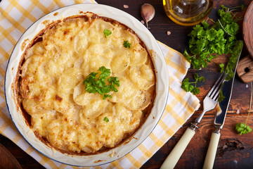 Potato gratin. Slices of potato backed with cream sauce, garlic and cheese, decorated with parsley leafs. Top view. Rustic style. Vegetarian dish.