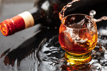 Bottle of red wine with wineglass. Water splash and droplet on the black reflection.