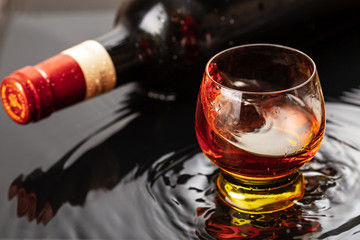 Bottle of red wine with wineglass. Water splash and droplet on the black reflection.