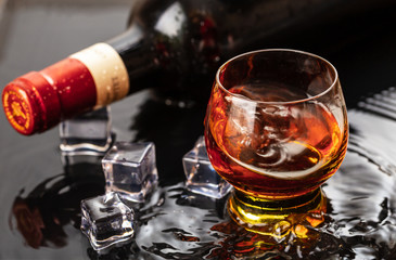 Bottle of red wine with wineglass. Water splash and droplet on the black reflection.