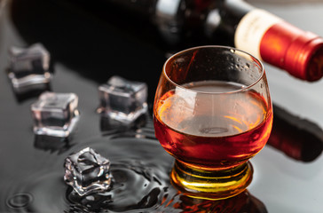 Bottle of red wine with wineglass. Water splash and droplet on the black reflection.